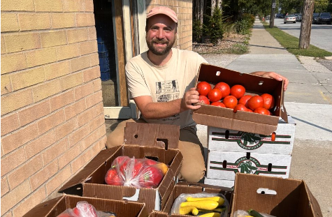  Will Moyer the Food Hub Man年龄r at 阿格斯农场站 st和s behind several boxes of produce